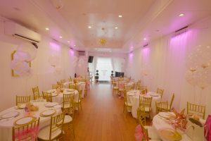 Walk into elegance at Queens Party Hall! This baby shower layout features gold chairs, soft pink lighting, and adorable teddy bear centerpieces for a warm, welcoming vibe.