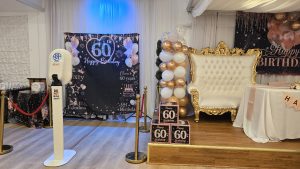 Stunning birthday stage setup with an ornate gold throne chair, rose gold and white balloon garland, and custom “Happy 60th Birthday” backdrop, creating the perfect focal point for memorable photos.